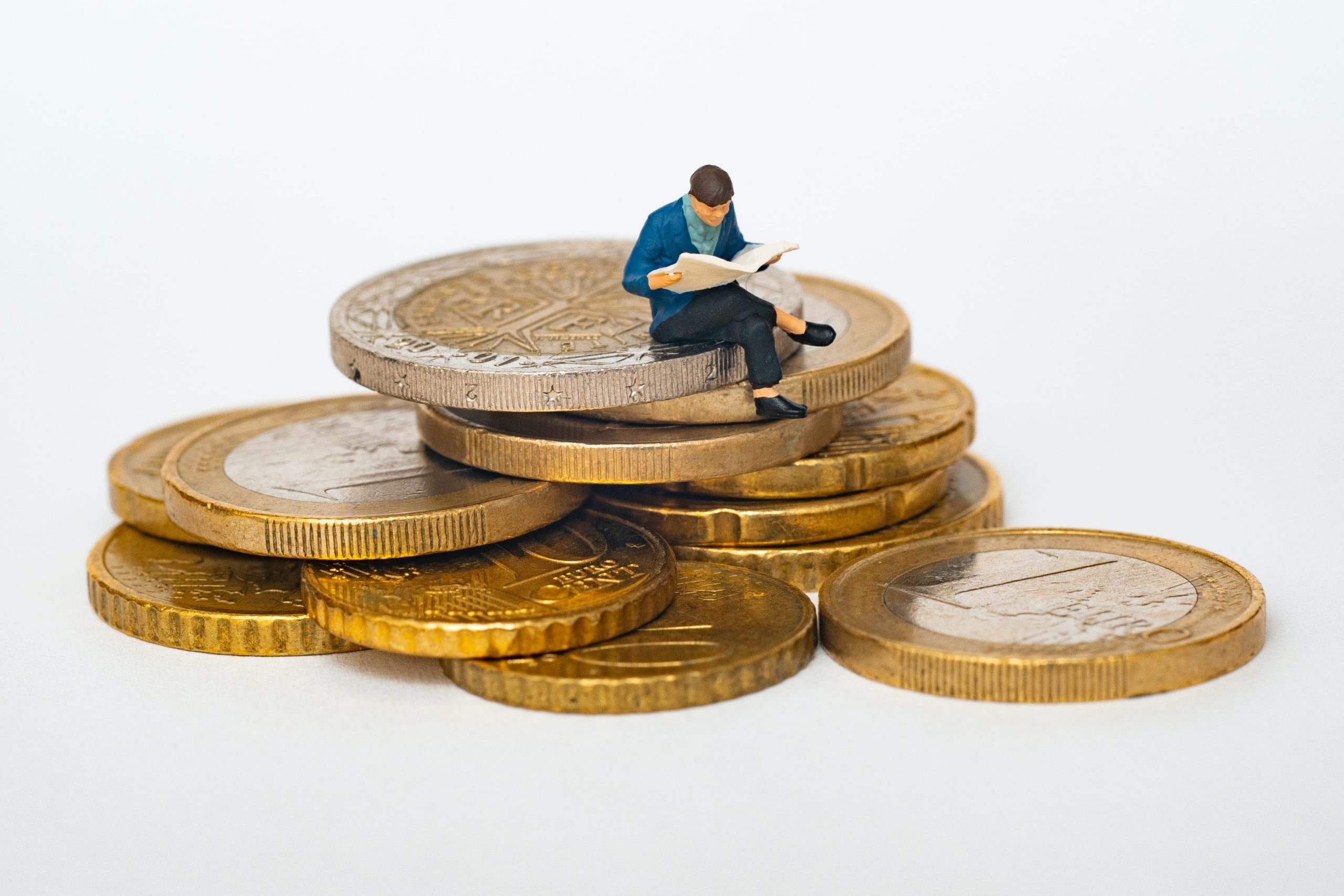 Miniature d'homme lisant sur une pile de pièces d'euro.